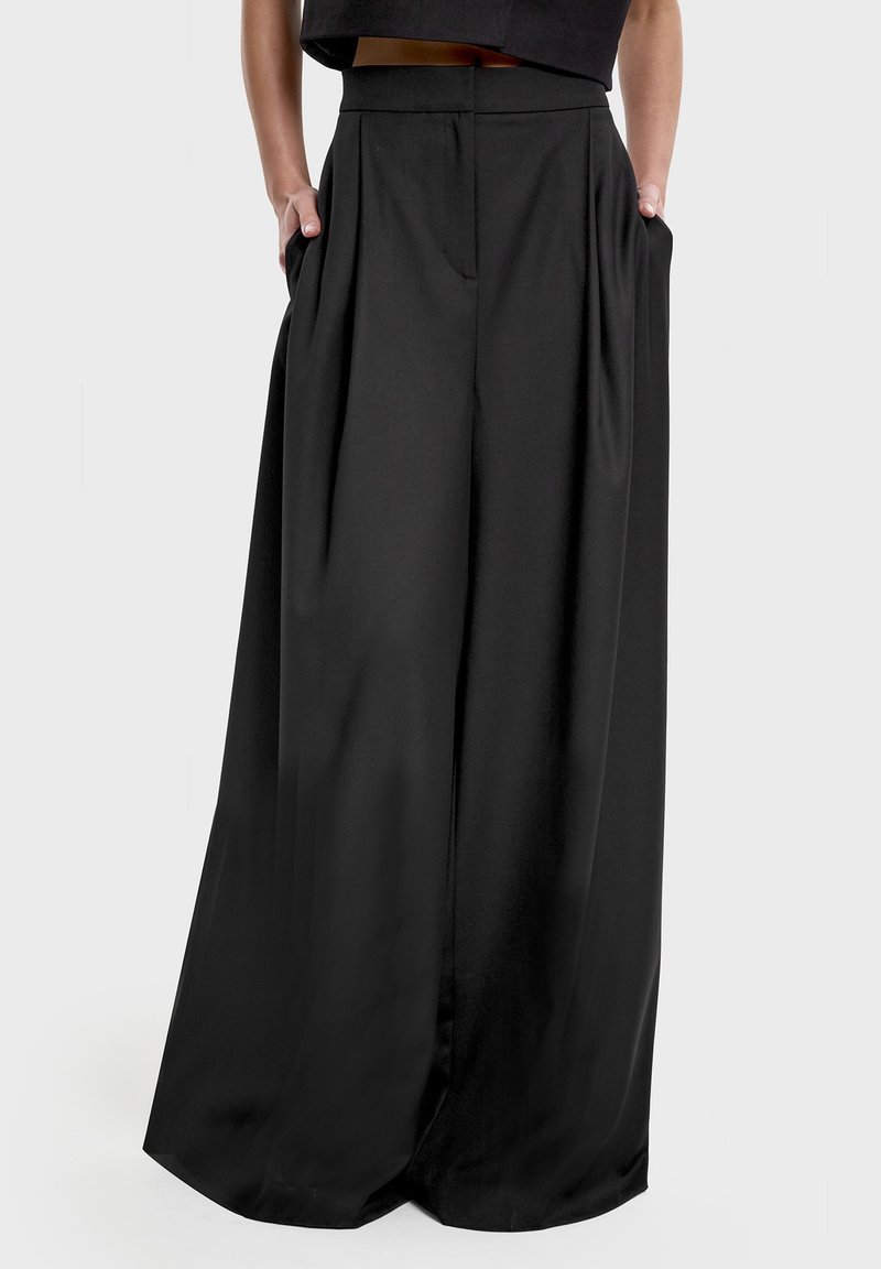 Szerokie czarne spodnie z wysokim pasem, wykonane z gładkiego materiału. Posiadają boczne kieszenie i pionowe przymarszczenia dla dodatkowego charakteru.