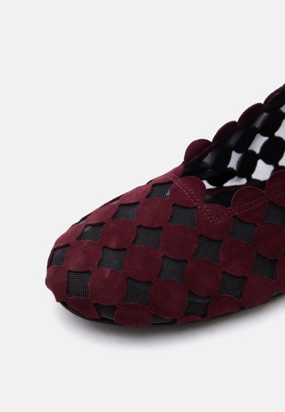 Πλατιά παπούτσια με επικάλυψη από σκουρόχρωμο κόκκινο σουέτ, με στρογγυλεμένες λουλουδένιες κοψίματα που αποκαλύπτουν μαύρο τούλι από κάτω.