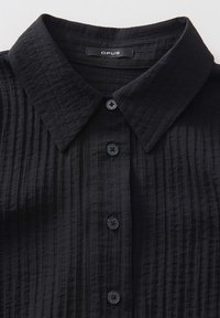Camicia nera in tessuto texture con colletto button-down, caratterizzata da cinque bottoni abbinati e un sottile motivo a righe su tutta la stoffa.