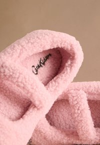 Ružové, chlpaté papuče vyrobené z mäkkých, textúrovaných materiálov s dizajnom prekrytého remienka. Vo vnútri je prešívané logo.