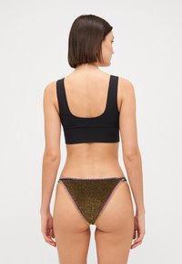 Top da bagno nero corto abbinato a slip bikini dorati glitterati con cuciture multicolori lungo i bordi. Texture liscia e vestibilità aderente.