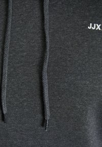 Grå hettegenser med teksturert stoff, snor med flettet design, og en liten hvit logo på fronten.