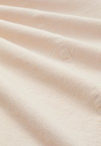 Tissu beige clair doux avec une texture visible de tissage fin et des lignes de couture diagonales subtiles créant des plis délicats.