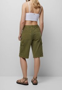 Shorts cargo vert olive avec deux poches latérales et poches arrière, associés à un crop top blanc froncé. Des sandales à lanières simples complètent le look.