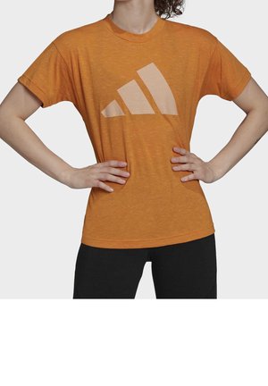 Oranžové tričko s krátkým rukávem vyrobené z texturované tkaniny, se velkým světle béžovým logem Adidas na přední straně a klasickým kulatým výstřihem.
