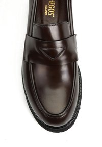 Brązowy skórzany mokasyn z okrągłym czubkiem, z szerokim paskiem i subtelnym trójkątnym wycięciem. Podeszwa jest z fakturowanej czarnej gumy.