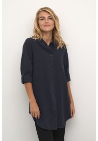 Laivastonsininen nappikauluspaita, pitkät hihat, joissa käännökset hihansuissa, ja yksi rintatasku. Silkkinen rakenne, rento muotoilu.