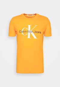Oranžové bavlněné tričko s kulatým výstřihem, krátkými rukávy a bílým logem "CK" s nápisem "Calvin Klein Jeans" v černé barvě pod logem.