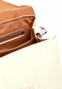 Borsa in pelle color crema aperta per mostrare l'interno in tessuto marrone con tasca con cerniera e anello metallico argentato sull'attacco della tracolla.
