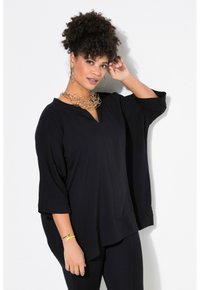 Blusa nera oversize con scollatura a V e maniche larghe fino al gomito. Tessuto morbido con una vestibilità rilassata, abbinata a una collana d'oro di grande impatto.