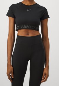 Top atlético negro recortado con mangas cortas, que presenta un logo blanco de Nike y una cinturilla texturizada con la inscripción "Nike Pro".