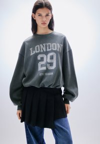 Antrasiitinharmaa collegepaita, jossa valkoinen "LONDON 29 ATH SEASON" -painatus. Mallissa on ylisuurennetut hihat, resorikaulus ja rento istuvuus.