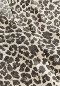 Leopardenmuster-Stoff mit einer strukturierten Oberfläche und dunklen Flecken auf einem hellbeigen Hintergrund, der ein weiches Gefühl und einen fließenden Fall zeigt.