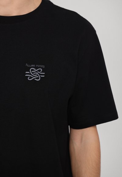 Black cotton t-shirt with short sleeves and a round neck, featuring a small gray embroidered logo on the left chest area.
