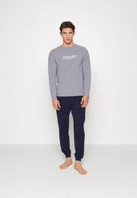 Grå langermet skjorte med "JOOP!" trykket i hvitt, kombinert med mørkeblå joggebukser; minimalistisk design, bomullsblanding, avslappet passform.