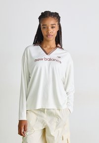 Weißes langärmliges Mesh-Oberteil mit braunem Kragen und "new balance"-Logo auf der Vorderseite. Verfügt über einen lockeren Schnitt und ein V-Ausschnitt-Design.