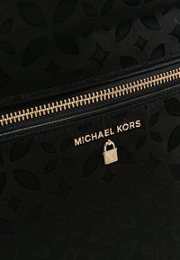 Tissu noir texturé avec motif floral, fermeture éclair dorée et logo Michael Kors doré avec détail cadenas.
