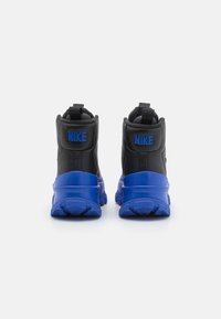 Juodos ir mėlynos „Nike“ sportbačiai su aukštu designu. Yra juodos odos viršus, mėlynas guminis padas ir mėlynas „NIKE“ logotipas.