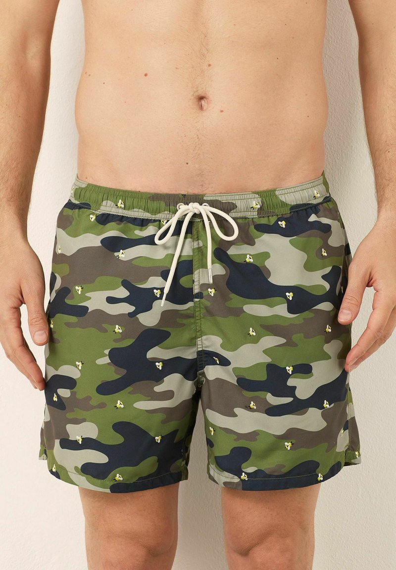 Costumi da bagno mimetici con motivi verdi, grigi e neri, arricchiti da piccoli fiori gialli. Vita elastica con coulisse.