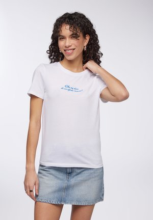 T-shirt bianco in cotone con maniche corte, con testo blu sul petto. Abbinato a una gonna di jeans, che mostra un look casual.