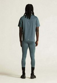 Athletic outfit met een teal T-shirt en nauwsluitende teal leggings. Het T-shirt heeft korte mouwen en de leggings reiken tot de enkel.