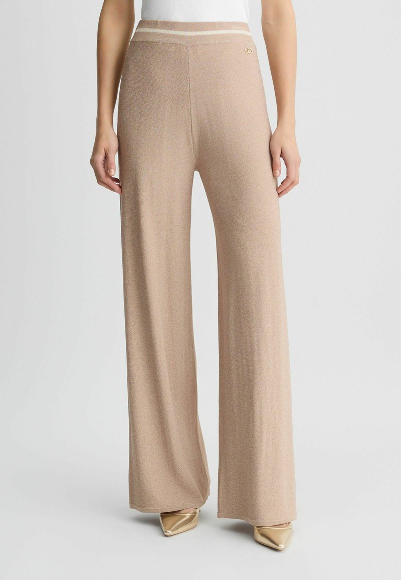 Beige, hoch taillierte, weite Hosen aus einem weichen, strukturierten Stoff. Sie verfügen über einen gestreiften Bund und ein dezentes Logo-Detail an der Seite.