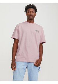 Lyserød bomulds T-shirt med korte ærmer, rund hals, der har et lille trykt logo på venstre bryst. Båret sammen med lyseblå denim jeans.