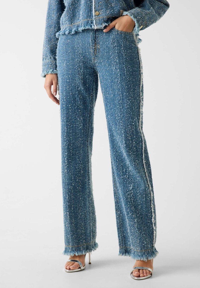 Pantaloni a gamba larga in tweed blu con orlo sfrangiato e dettaglio di striscia laterale bianca. Il tessuto è strutturato con filati di colori variabili.