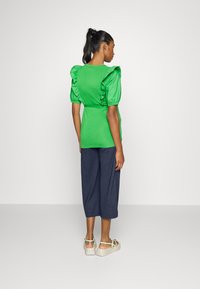 Top verde de manga curta com mangas franzidas, cintura ajustada, combinado com culotes largos azul-marinho e sandálias de plataforma leves. Conjunto simples e casual.
