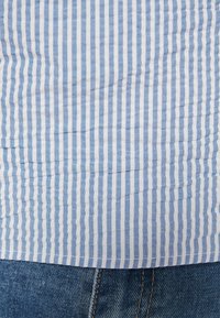 Tecido listrado azul e branco com um acabamento texturizado, drapeado sobre um tecido de denim com costuras visíveis.