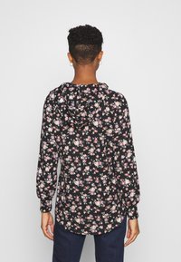 Sweat à capuche noir à fleurs avec manches longues, présentant de petites fleurs roses et blanches, texture douce, et un ourlet arrondi. Capuche visible à l'arrière.