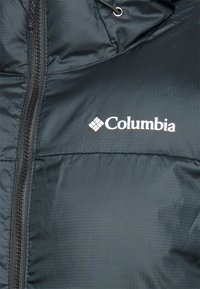 Chaqueta de plumas negra con una superficie lisa y texturizada. Cuenta con un cierre de cremallera y el logo de Columbia en blanco en la zona del pecho.