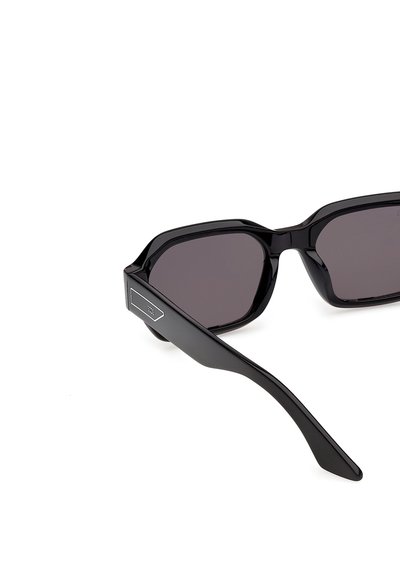 Gafas de sol rectangulares negras con lentes tintadas oscuras y varillas rectas y gruesas que presentan una pequeña placa con el logo metálico.