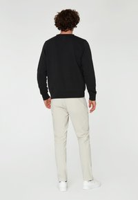 Felpa nera con scollatura rotonda, polsini e orlo a coste; abbinata a pantaloni beige chiaro e sneakers bianche. Vestibilità casual e comoda.