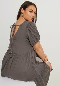 Vestido gris texturizado con mangas abullonadas, espalda baja y cierre de lazo. Presenta una falda fluida y bolsillos laterales.