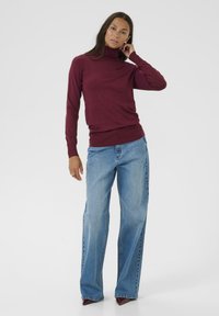 Burgundin turtleneck-neule pehmeästä kankaasta, yhdistettynä vaaleansinisiin leveälahkeisiin farkkuihin. Asusteessa on tyylikäs, vartalonmyötäinen siluetti.