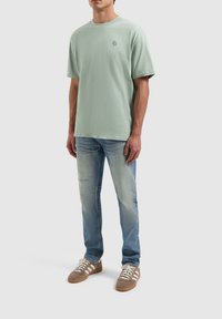 Mintgroene katoenen t-shirt met een ronde hals en een klein logo op de borst, gecombineerd met lichtblauwe denim jeans en bruine sneakers.