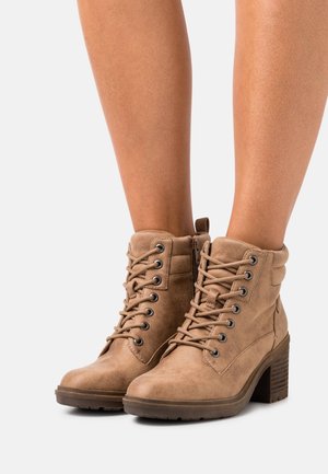 Béžové semišové kotníkové boty se šněrováním vpředu a bočním zipem, mají strukturovaný povrch a robustní podpatek. Kování zahrnuje kulaté průchodky.