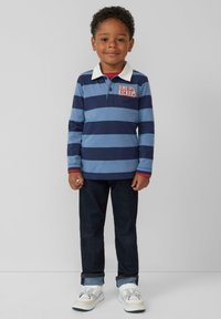 Blauw en marine gestreepte long-sleeve polo met witte kraag en "DINO KICKERS" graphic, gecombineerd met donkere denim jeans en witte sneakers.