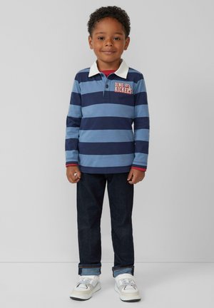 Blauw en marine gestreepte long-sleeve polo met witte kraag en "DINO KICKERS" graphic, gecombineerd met donkere denim jeans en witte sneakers.