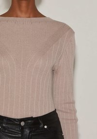 Ribbade stickade tröja i mjuk beige med en vid halsringning och tight passform, med diagonala sömdetaljer och långa ärmar. Kombinerad med svarta byxor.