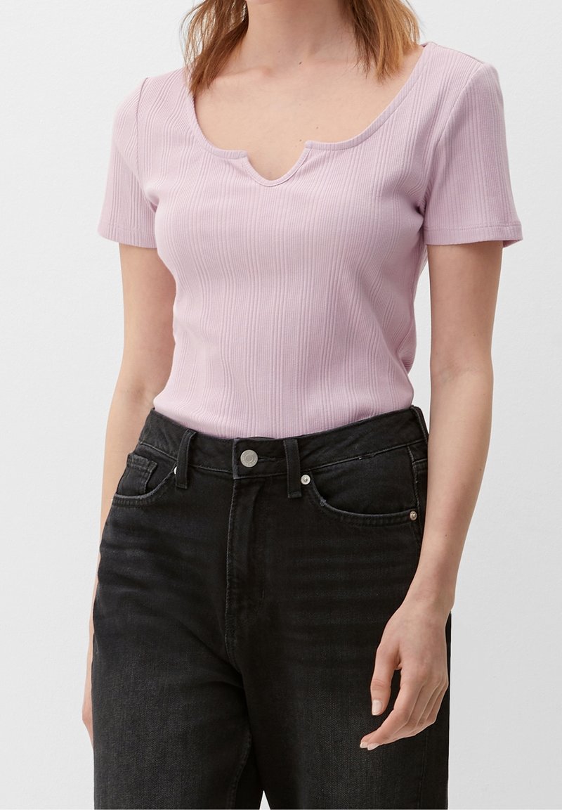 Femme portant un haut à manches courtes côtelé violet clair avec une encolure arrondie à encoches et un jean noir taille haute.