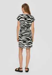Zebraprint jurk in zwart-wit met korte fluttermouwen, een strakke taille en een knielange zoom, gecombineerd met zwarte sandalen.