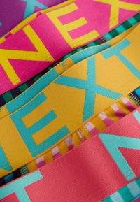 Colorful elastic bands in pink, yellow, and blue featuring large, bold letters. Textured fabric with varying widths and patterns visible.