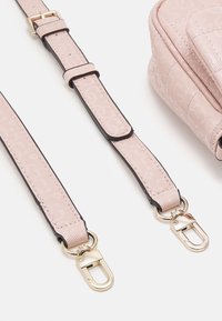 Pasek do torebki na ramię w jasnoróżowym materiale z subtelnym wzorem logo, z elementami w złotym odcieniu i czarnymi akcentami na krawędziach.