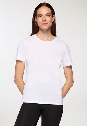 T-shirt bianco a maniche corte realizzato in tessuto morbido, con scollatura tonda e taglio dritto, abbinato a leggings neri. Texture liscia, design semplice.