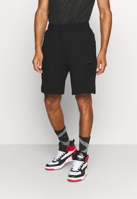 Černé sportovní kraťasy s elastickým pasem, mají boční kapsy a malé logo Puma. Spárovány s černobílými vysokými teniskami.