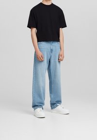 Svart kort t-shirt, ljusblå vida jeans och vita sneakers. Jeansen har en blekt tvätt och klassisk femficksdesign.