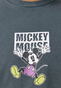 Šedé bavlněné tričko s potiskem Mickey Mouse v jasně žlutých botách a fialových šortkách, s tučným textem "MICKEY MOUSE."