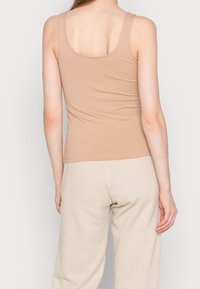 Naken linne i mjukt, stretchigt material med breda axelremmar och en tajt design, parat med ljusbeige träningstype.